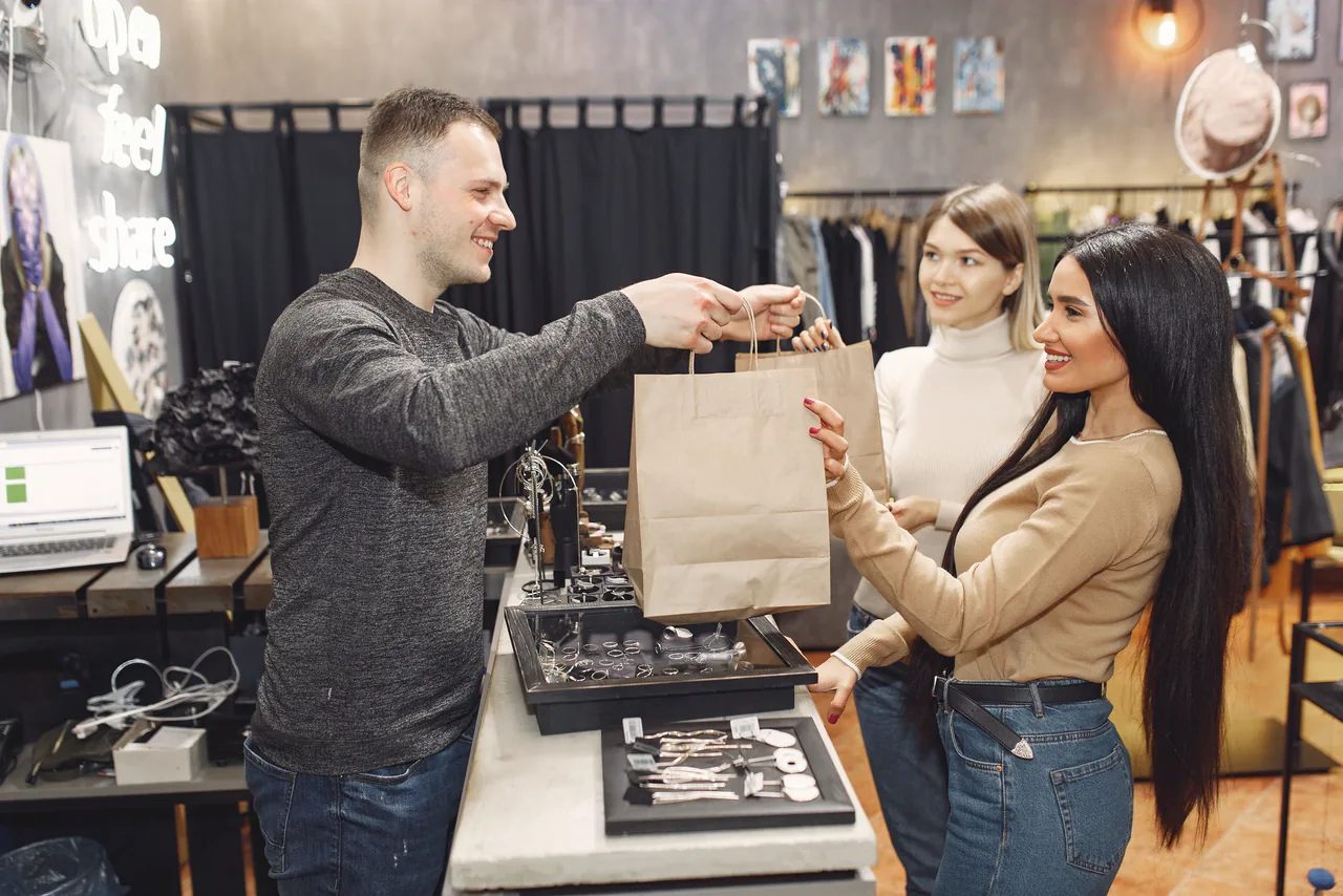 A shopkeeper handing shopping bags to two smiling customers